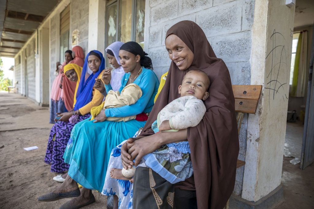 Women are waiting in front of the health centre with their children.