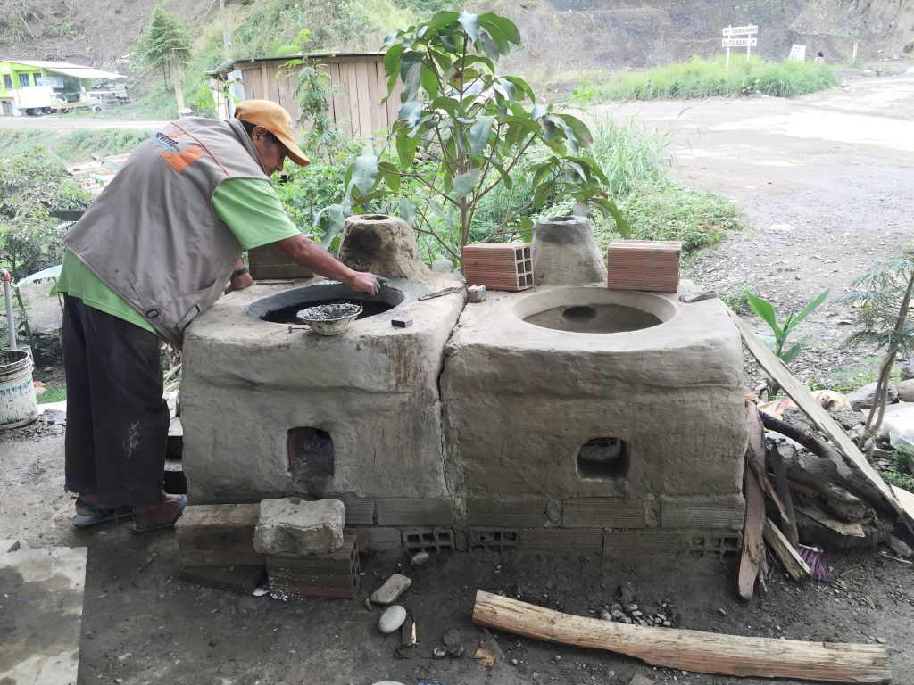 A Bolivian man is working on two large clay cookstoves.