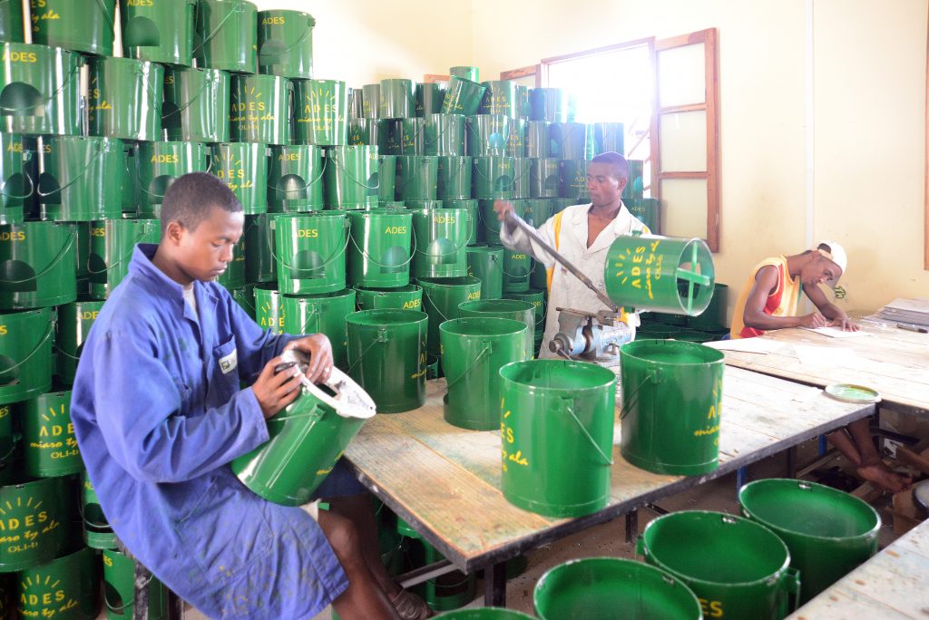 Three Madagascan men are working on green metal cauldrons with a yellow line saying "ADES" on them.