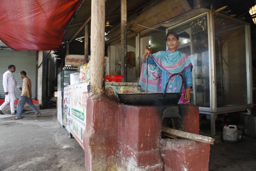 A Bangladeshan woman is cooking on a very large top on a clay stove.