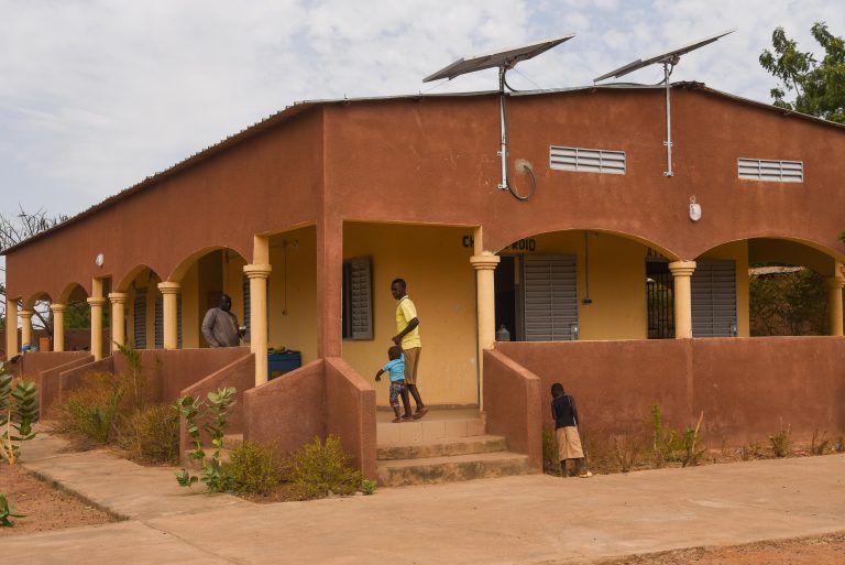 A man an a young boy are walking in front of a brown house with solar panels on top.