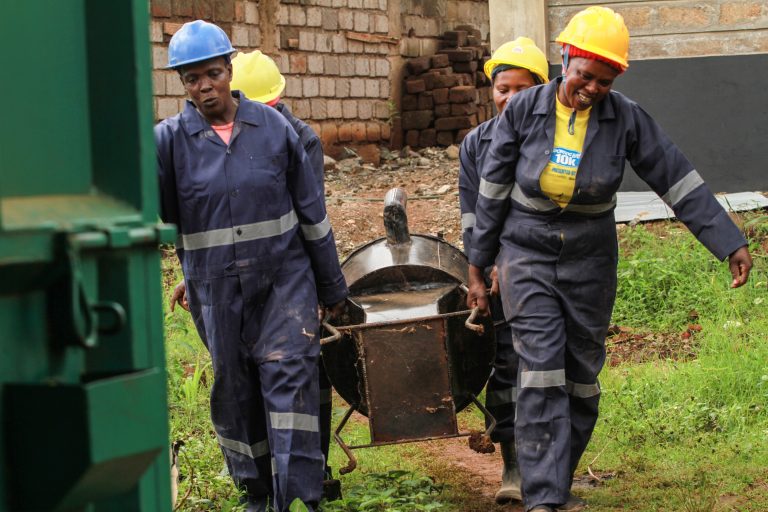 Four persons in workwear carry a cookstove.