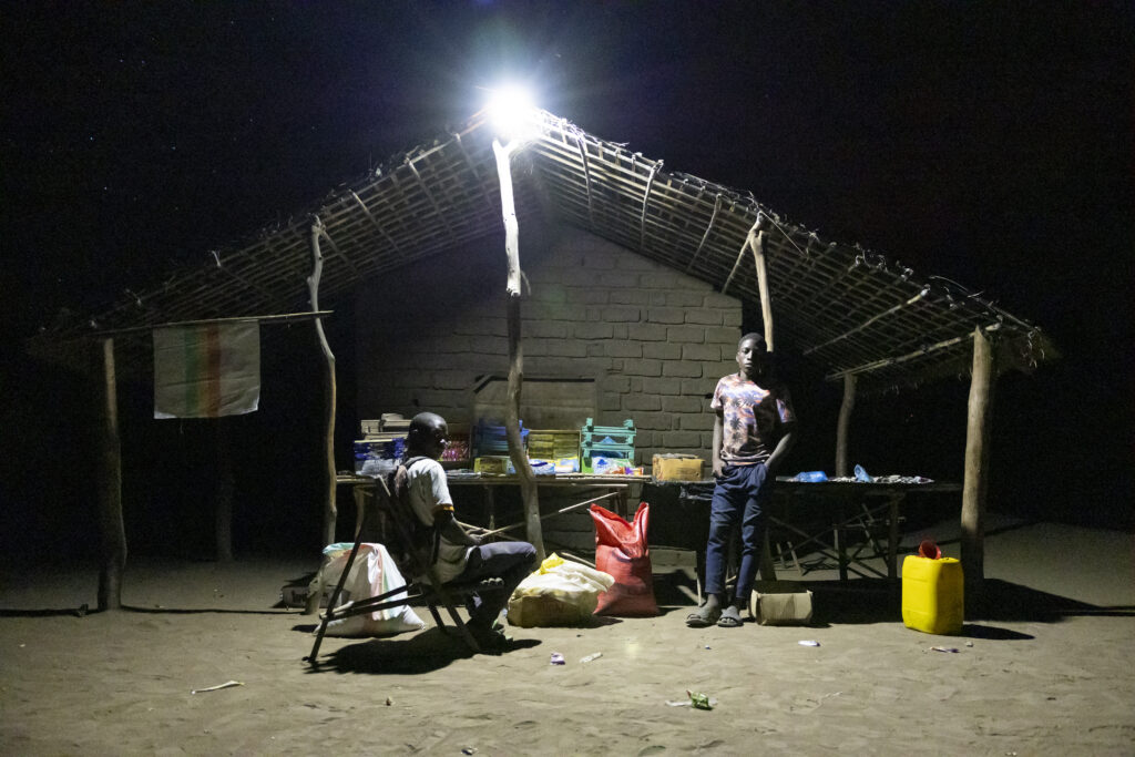 A brightly lit shop at night in a rural area, where access to energy sparks connection and commerce.